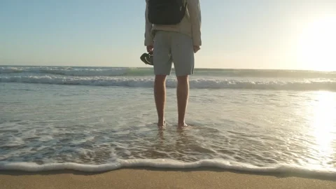 Young man standing on a sandy ocean beach at a beautiful summer sunset Stock Footage 303047298