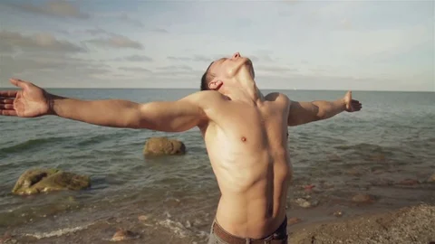 A young man is standing on the seashore with arms outstretched. 스톡 동영상 78712389