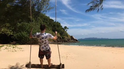 Young Man standing on a Swing on the Beach in Mu Ko Lanta National Park Stock Footage 124327703