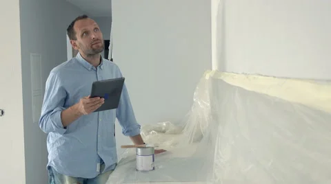 Young man standing with tablet during painting wall in his new home, 4K Stock Footage 64550360