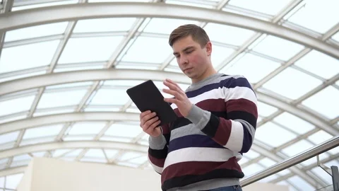 A young man is standing with a tablet. A man uses a tablet against a pan-glass Stock Footage 127393903