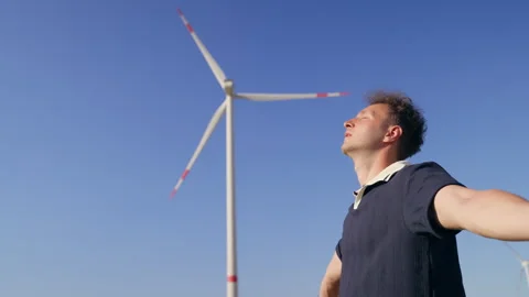 Young Man Standing Under a Wind Turbine Looking Up at Clear Blue Sky Stock Footage 340108191