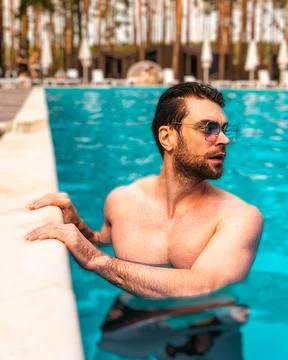 Young man standing in the water while having rest in the swimming pool outdoors Stock Photos