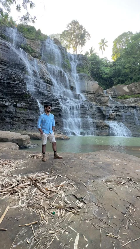 Young Man Standing by Waterfall, Lush Green Jungle Landscape, Vertical Wide Shot Stock Footage 324770411