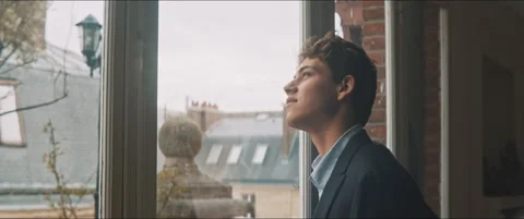 Young man standing by the window looking at the cloudy sky Stock Footage 203586387