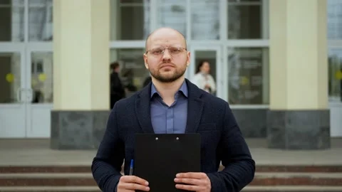 Young man stands against the background of the university with a folder in hands Stock Footage 192355451