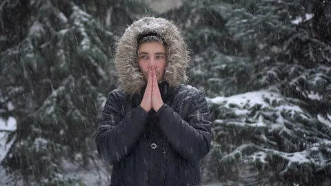 A young man stands against a background of fir trees under heavy snowfall and Stock Footage 256526358