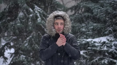 A young man stands against a background of fir trees under heavy snowfall and Stock Footage 257565983