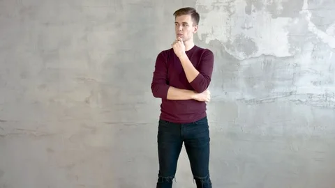 Young man stands on background of gray wall thinking about solving the problem Video stock 120168468