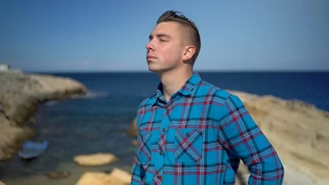 A young man stands on the background of the sea. A man in a blue shirt puts on Stock Footage 120147259