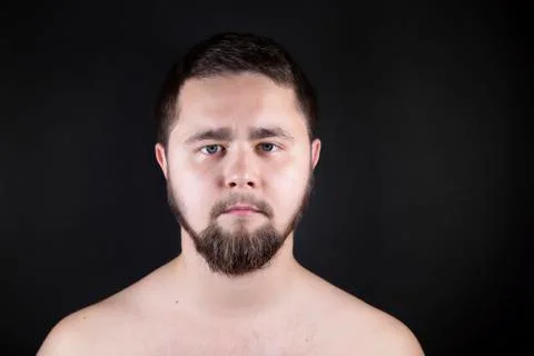 A young man stands with a bare torso on a black background. A man with a bear Stock Photos