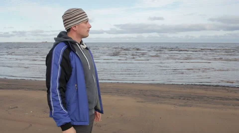 A young man stands on the beach and looks into the distance Video stock 56576667