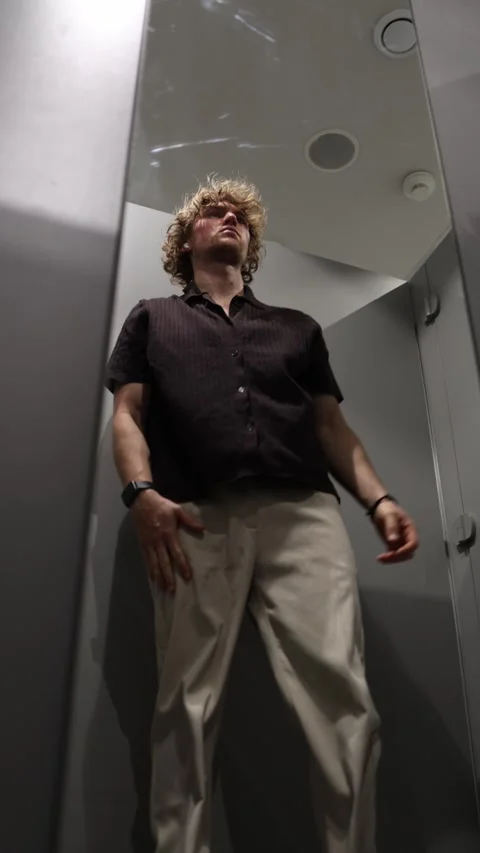 Young man stands to check his outfit in mirror then sits back down Stock Footage 344854699