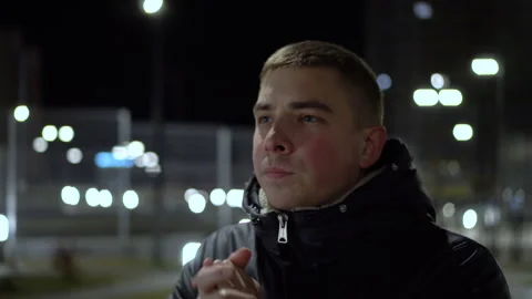 A young man stands in the cold in the evening outside and warms his hands with Stock Footage 142582165