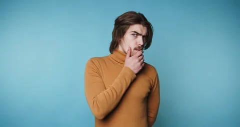 Young man stands in a contemplative pose with his hand on his chin, suggest.. Stock Footage 313280228