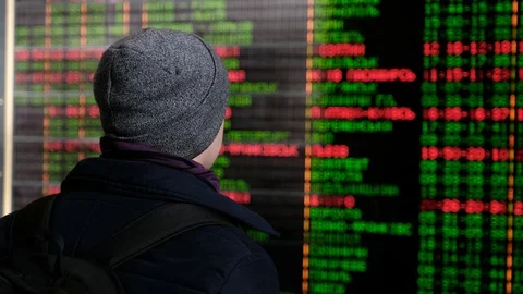 A young man stands by the electronic board of the schedule of arrival and Stock Footage 88299124