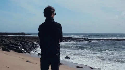 Young man stands on the empty sandy beach on the summer day and contemplati.. Video stock 240404117