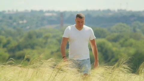 A young man stands in a field with open arms, gazing at the sunset and embracing Stock Footage 248319921