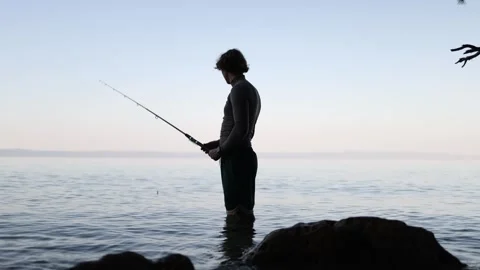 Young man stands knee deep in sea water preparing his fishing tackle Stock Footage 341622435