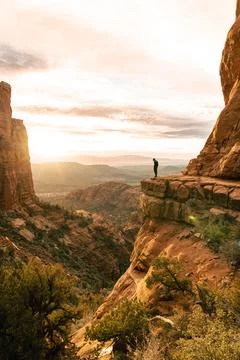 Young man stands looking down dramatic cliff at sunset at Cathedral Rock Sedo Stock Photos