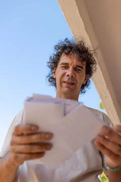 A young man stands at a mailbox with envelopes and reads a letter. Mail rec.. Stock Photos