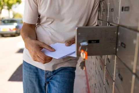 A young man stands at a mailbox with envelopes and reads a letter. Mail rec.. Stock Photos
