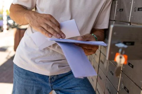 A young man stands at a mailbox with envelopes and reads a letter. Mail rec.. Stock Photos