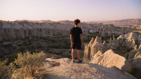 Young man stands on mountain top overlooking view and sunset Stock Footage 142550170