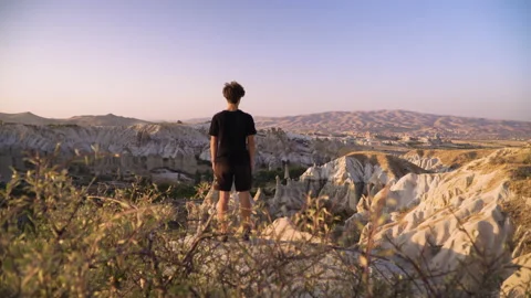 Young man stands on mountain top overlooking view and sunset Stock Footage 142550267