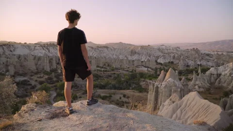 Young man stands on mountain top overlooking view and sunset Stock Footage 142550320