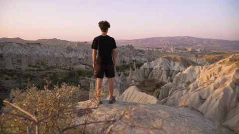 Young man stands on mountain top overlooking view and sunset Stock Footage 142550358