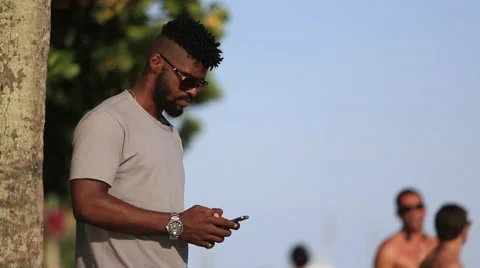 A young man stands outside by the beach and plays with his cell phone Stock-Footage 67347209
