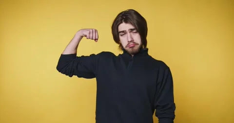 Young man stands with showing his muscles on yellow background Stock Footage 314336932