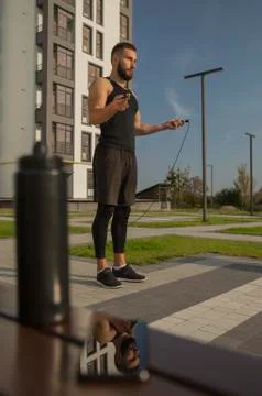 A young man stands with a skipping rope. Its display is in the smartphone. Stock Photos