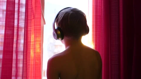 The young man stands by the window and dances, listening to music through Vidéo 87290007