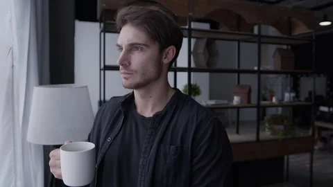 A young man stands by the window, drinks coffee, a girl approaches him, hugs Vidéo 129322566