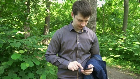 Young man stands in the woods, thinks about something and works on the phone Stock-Footage 77137286
