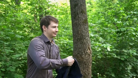 A young man stands in the woods,throws the jacket over his shoulder and makes a Stock Footage 77144894