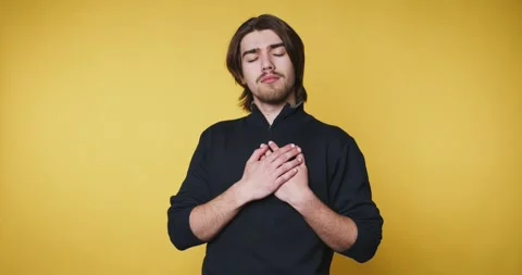 Young man stands on yellow background, placing his hands on his heart, conv.. Stock Footage 314337015