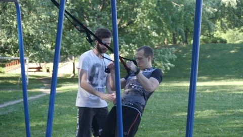 Young man starts doing pull-ups on fitness loops under control of bearded Video stock 99425455