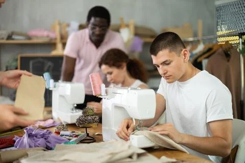 Young man stitching at machine during sewing class for adults Foto stock