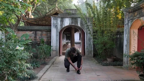 Young man stops to stoop down tying shoe laces before walking away Stock Footage 256736300