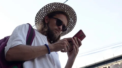 A young man in a straw hat and sunglasses is using his smartphone at the street. Stock Footage 107294907