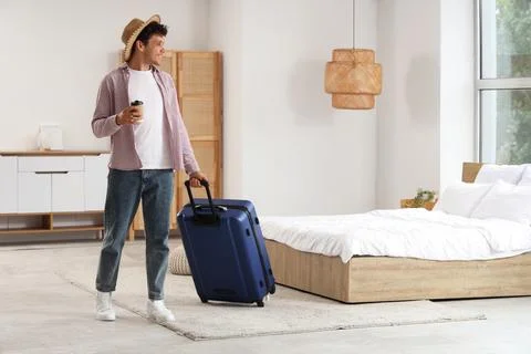Young man in a straw hat and casual clothes pulling a blue suitcase and holdi Stock Photos