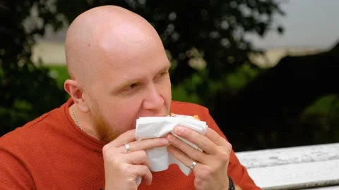A young man on the street eats a hamburger and wipes his mouth with a napkin. Stock Footage 139110883