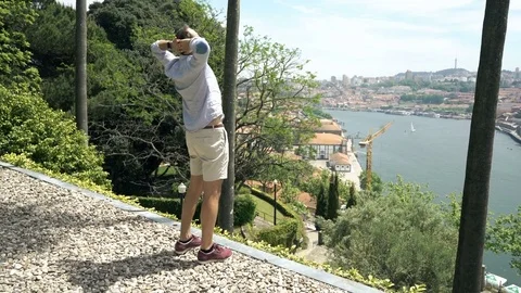 Young man stretching arms and admire view of Porto standing in garden Stock Footage
