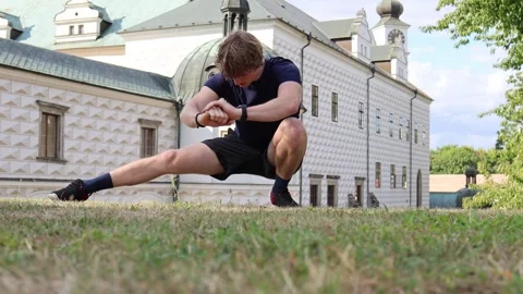 Young man stretching on grass in front of historic building warming up in the mo Vídeos de archivo 315413833