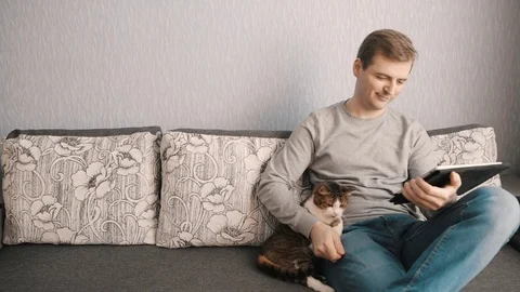 Young man stroking a cat and enjoys tablet Stock Footage 72620536