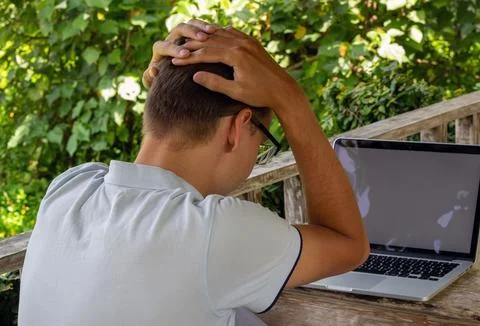A young man struggles with computer issues outdoors, adding to his frustration Stock Photos