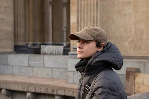 Young man student in brown cap and dark jacket gazes Stock Photos